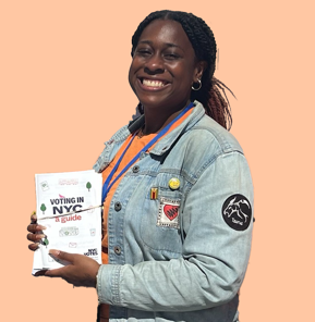 Amanda smiling while holding a flyer in front of an African American Day Parade backdrop.