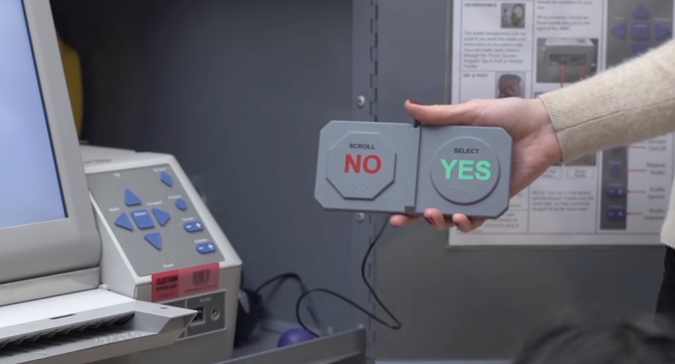 Poll worker presenting a Ballot Marking Device, with the options of NO in red and YES in green