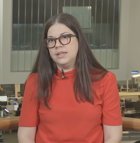 Allie Swatek, director of policy and research at CFB, wears a red shirt and glasses with her dark brown hair down as she speaks on NY1.​​ 