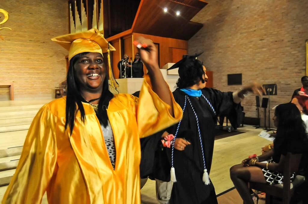 A woman smiling broadly in a bright yellow cap and gown at a College & Community Fellowship graduation ceremony.​​ 