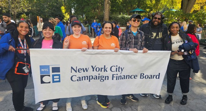 Un grupo de voluntarios y personal de la CFB sostienen una gran pancarta con el nombre y el logotipo de la agencia.