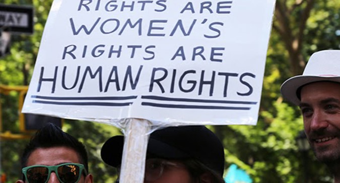 Un participant à la parade tient une pancarte sur laquelle on peut lire : « Les droits des personnes en situation de handicap sont des droits des femmes sont des droits humains ».