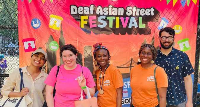Staff in front of a colorful sign reading: Deaf Asian Street Festival