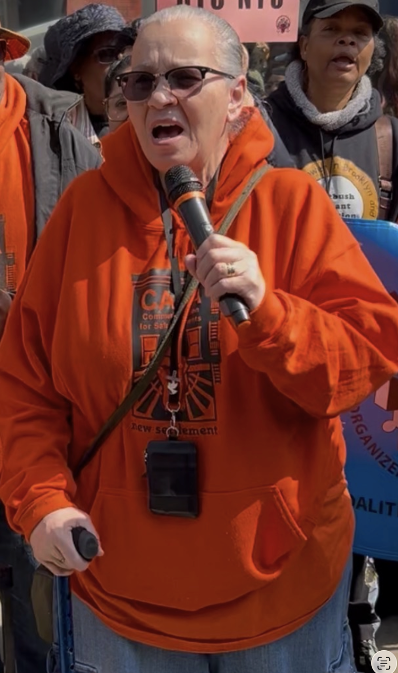 Pat Jewett speaking into a microphone at a CASA NYC event wearing an orange CASA hoodie.