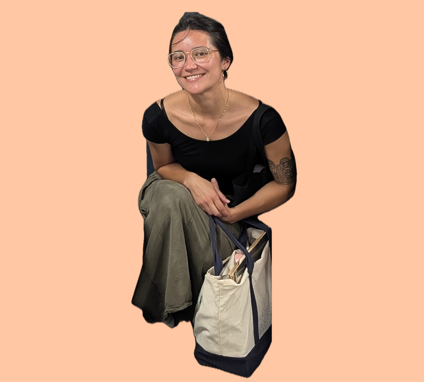 María, NYC Votes Youth Programs Coordinator, smiling while crouched, wearing a black top and olive pants, with a canvas tote bag beside her.